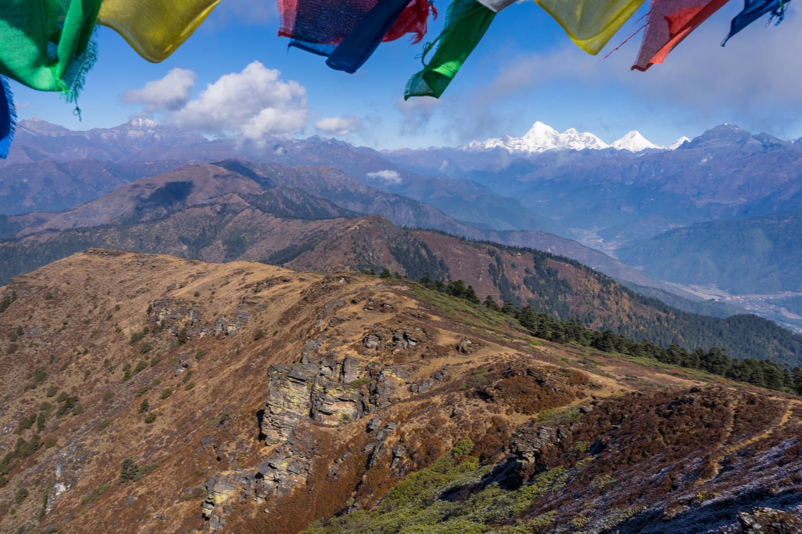 A ridge trail with prayer flags and Himalayan peaks beyond