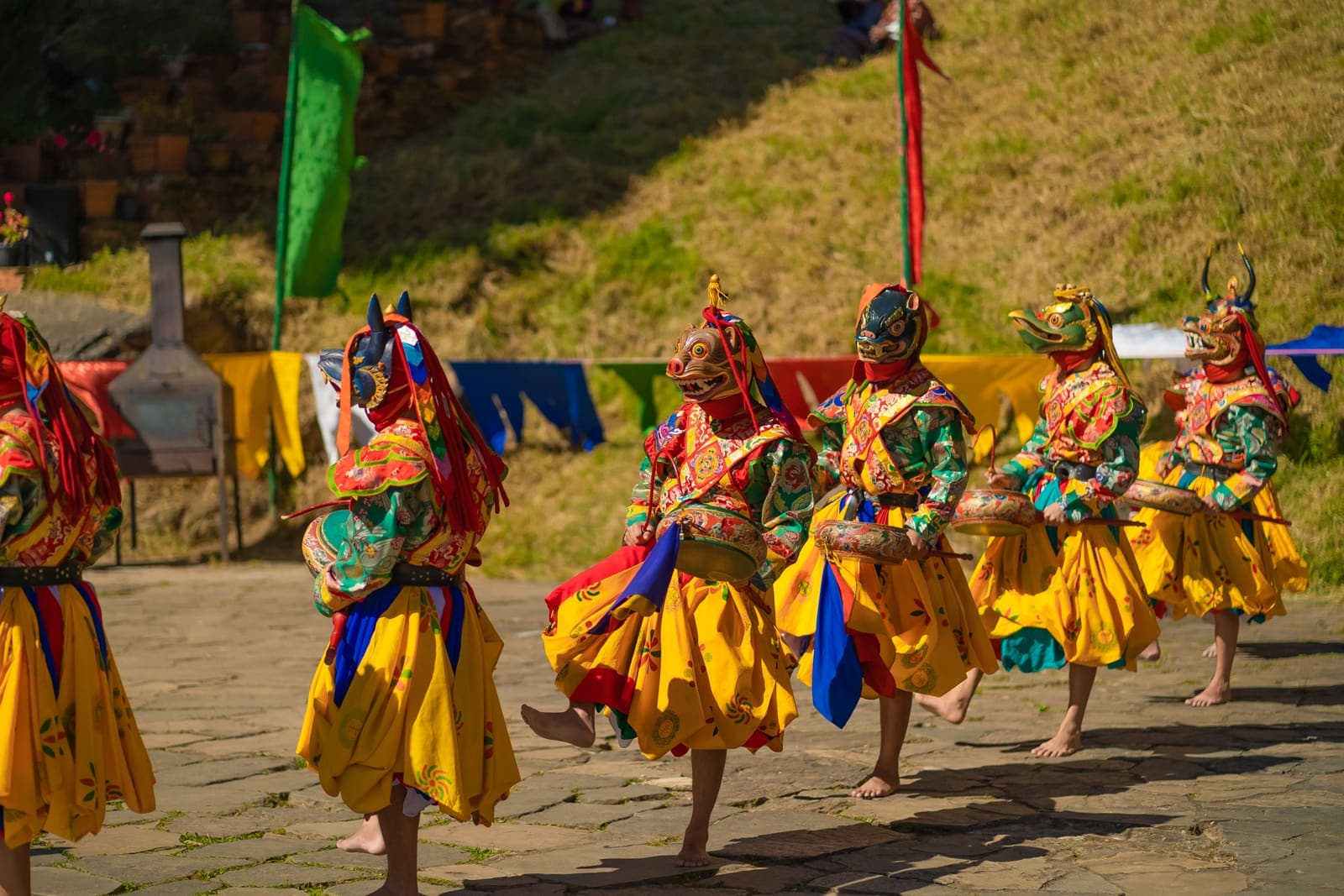 Masked dancers in yellow and green costumes at a tshechu