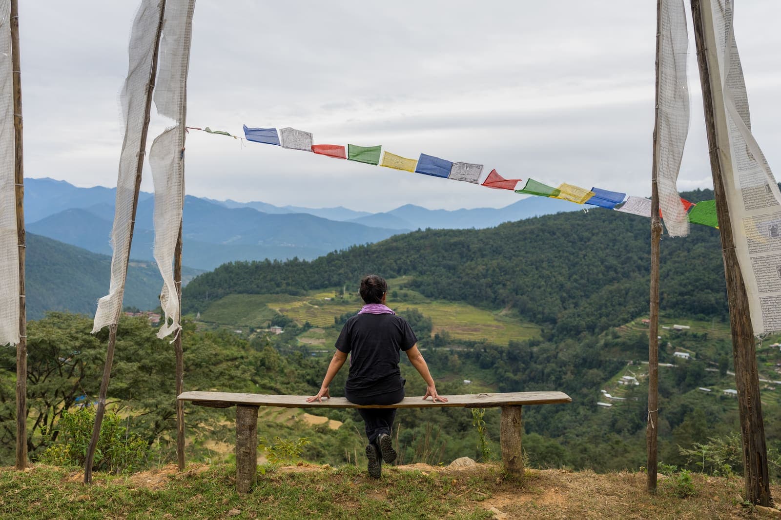A traveller resting on a bench beneath prayer flags