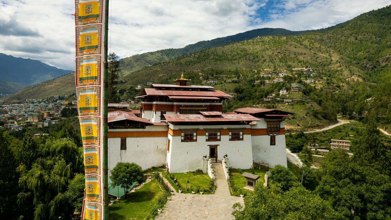 A traditional dzong with a tall prayer flag above the Thimphu valley