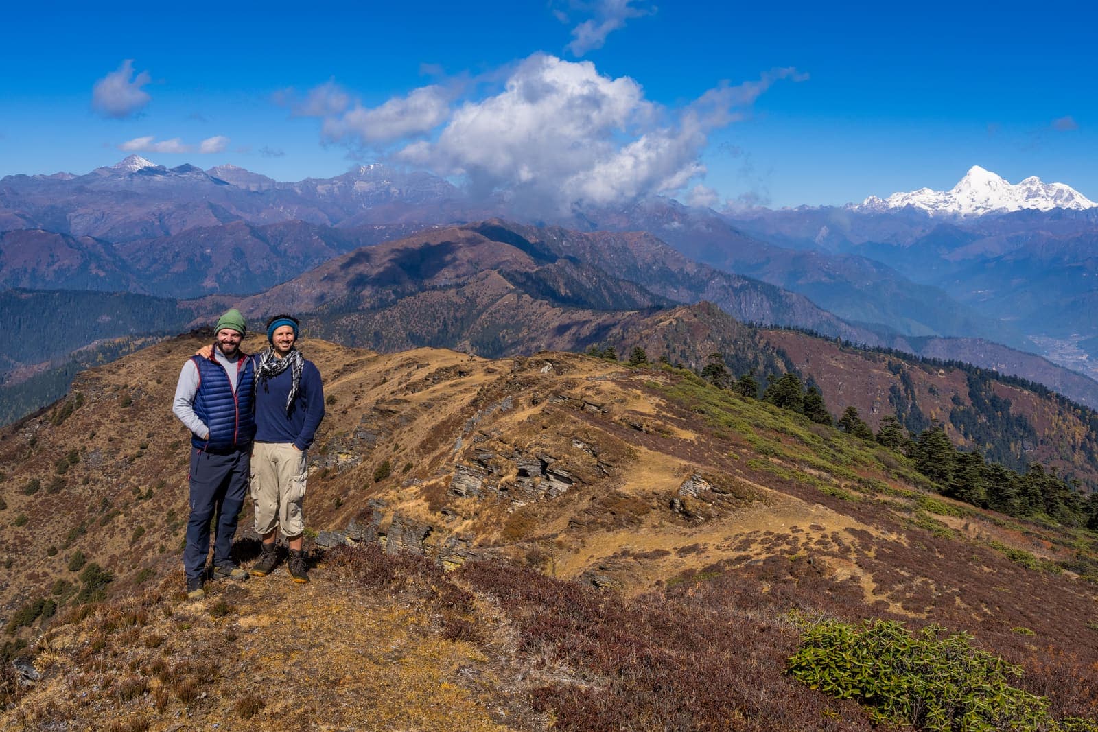 Two trekkers on a high ridge with snow peaks on the horizon
